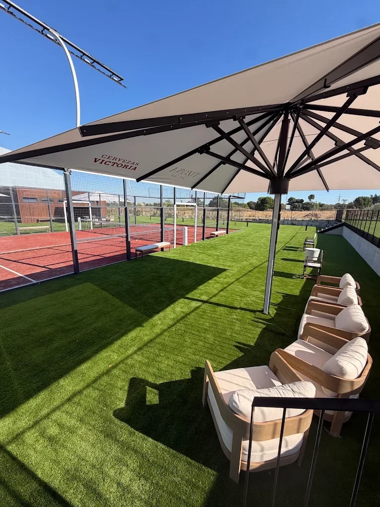 Outdoor armchairs beneath an umbrella beside Tizona’s padel court
